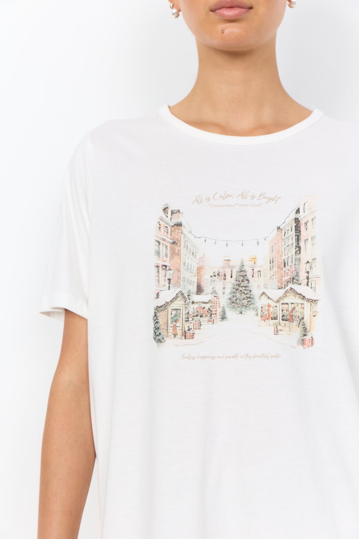 Modell bär vit t-shirt med julillustrerad tryck av vintrig stadsplats och text framifrån | Soya Concept | Lilla Hem