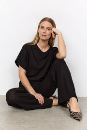 Modell sitter på golvet och bär svart ribbad t-shirt och byxor med v-ringning | Soya Concept | Lilla Hem