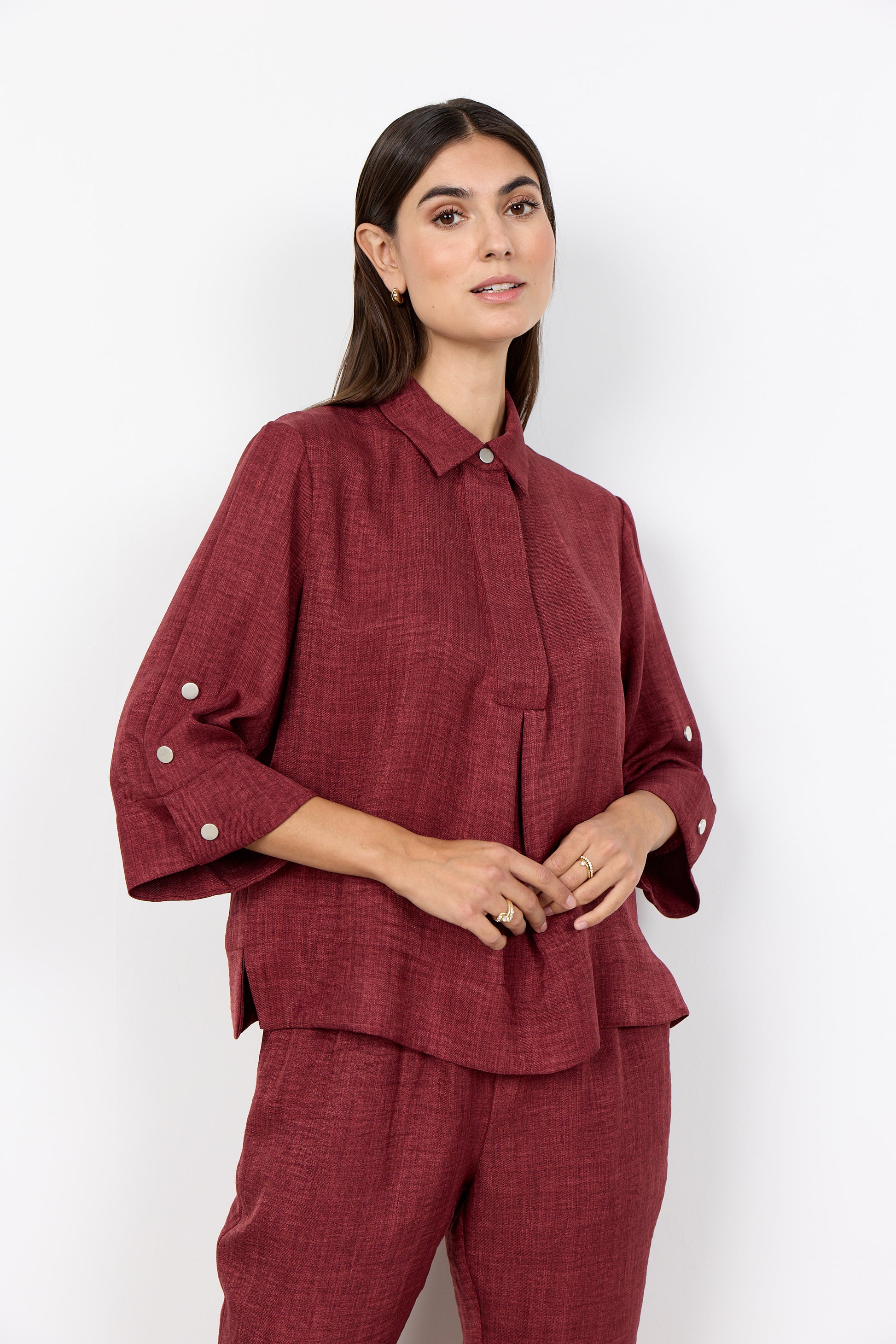 Modell bär burgundy linneskjorta framifrån med knappdetaljer på ärmarna