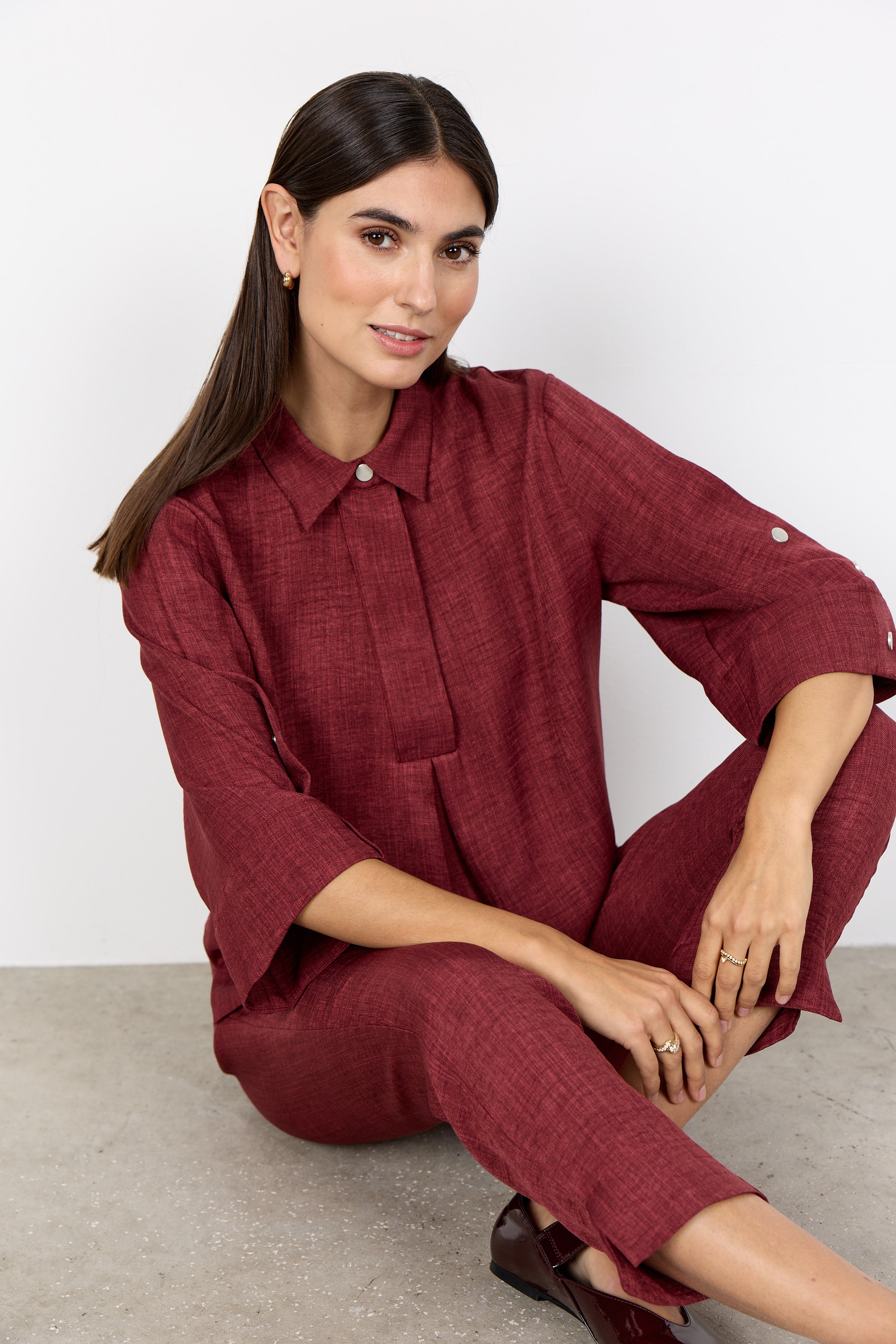 Modell bär burgundy skjorta och byxor i linneväv, sittande framifrån mot neutral bakgrund | Soya Concept | Lilla Hem